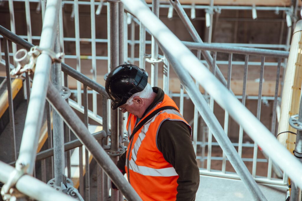 photo of construction worker wearing hard hat walking among metal pipes