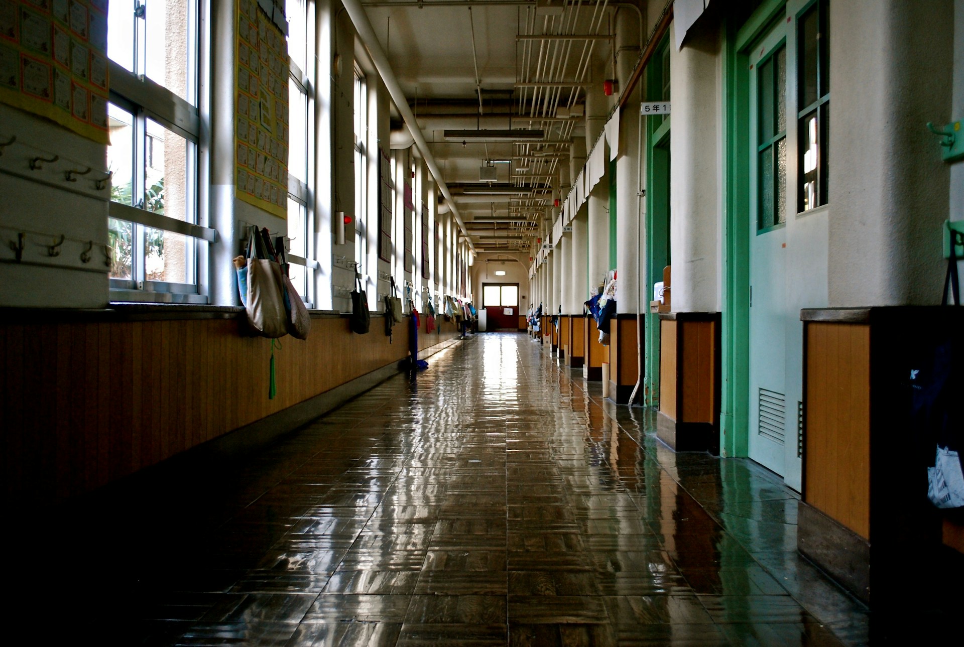 A school hallway with green classroom doors on one side, windows and school bags on hooks on the other, and the exit at the far end, representing schoolyard personal injury.
