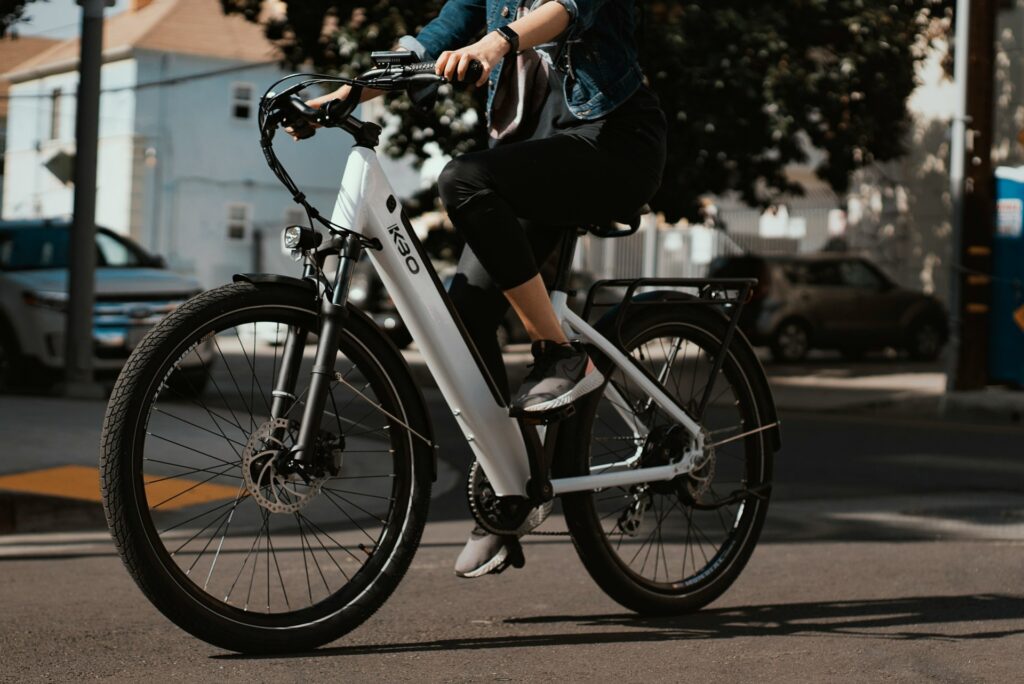 A woman, shown from the shoulders down, rides an e-bike down a city street, with blurred buildings and trees in the background, representing e-bike risks and liability in Ontario.