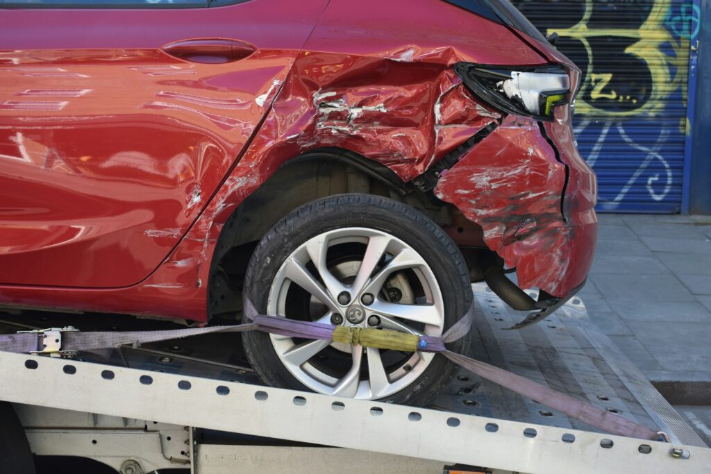 The damaged rear corner of a red car with the wheel strapped to a tow truck bed after a car accident that could result in complex regional pain syndrome.