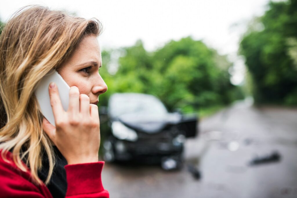 A woman on her cell phone with a car blurred in the background that appears to have been in a car accident in Ontario.