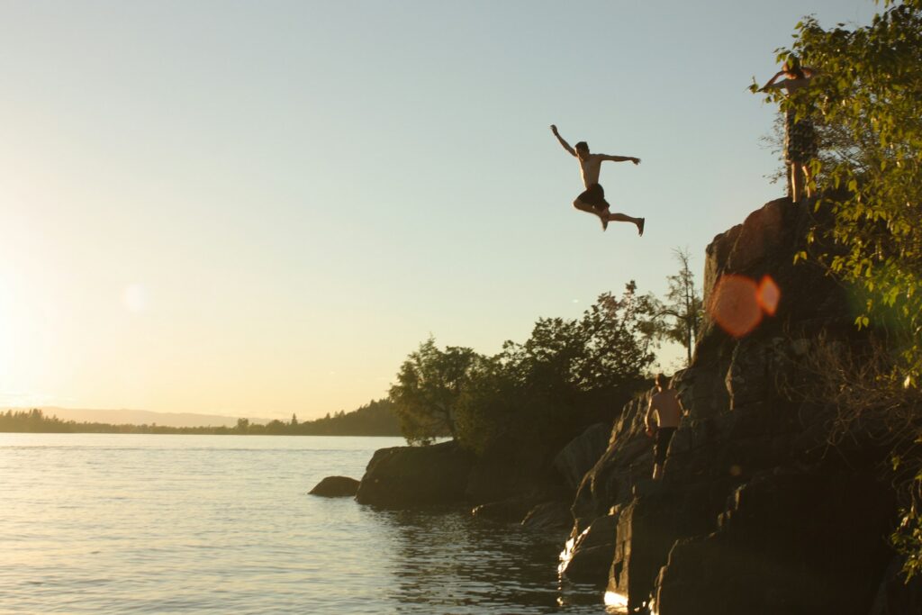 A person jumping off a rock cliff into a lake representing drowning risks at Ontario cottages.
