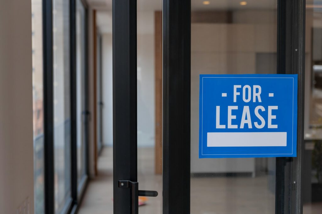 A blue for lease sign hangs in a window representing landlord defaults on a mortgage.